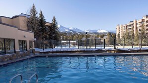 Une piscine à l’eau claire, entourée de bâtiments et avec, en arrière-plan, des montagnes enneigées.