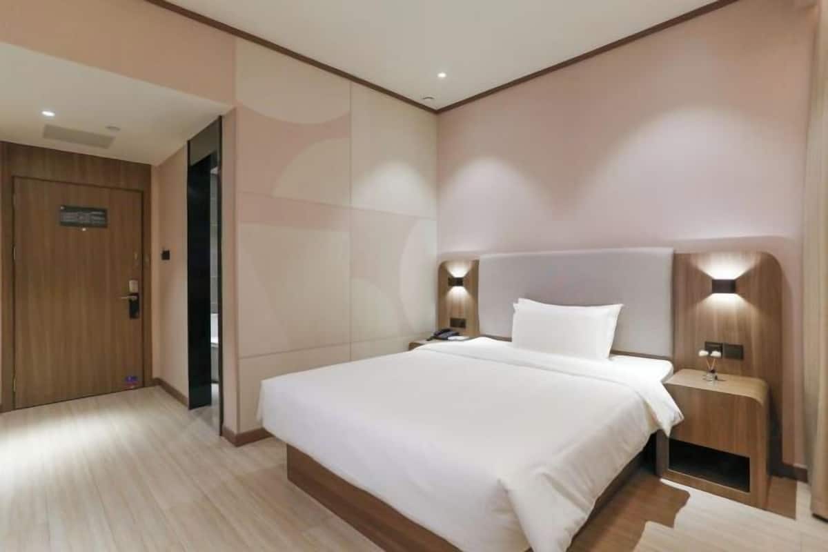 Una habitación de hotel moderna con una cama grande, cabecero de madera, lámparas de noche y una puerta de madera.