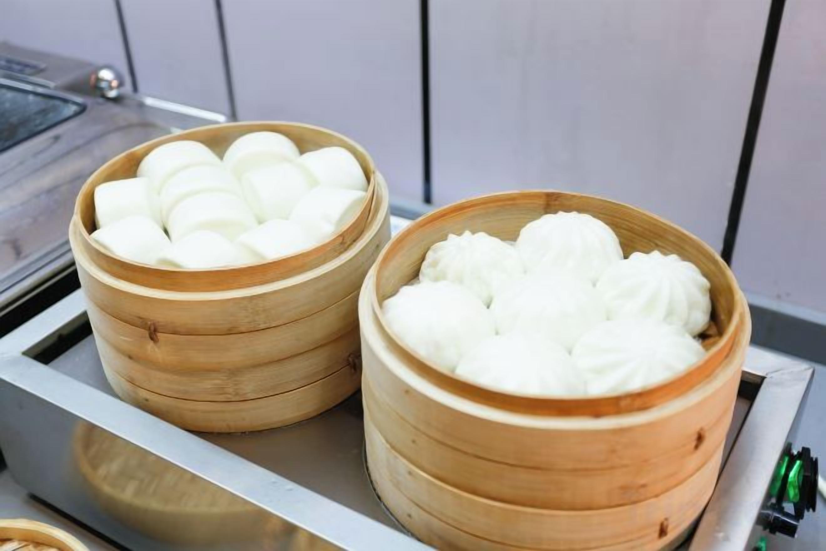 Two bamboo steamers with white food items, likely dumplings, on a metal tray.