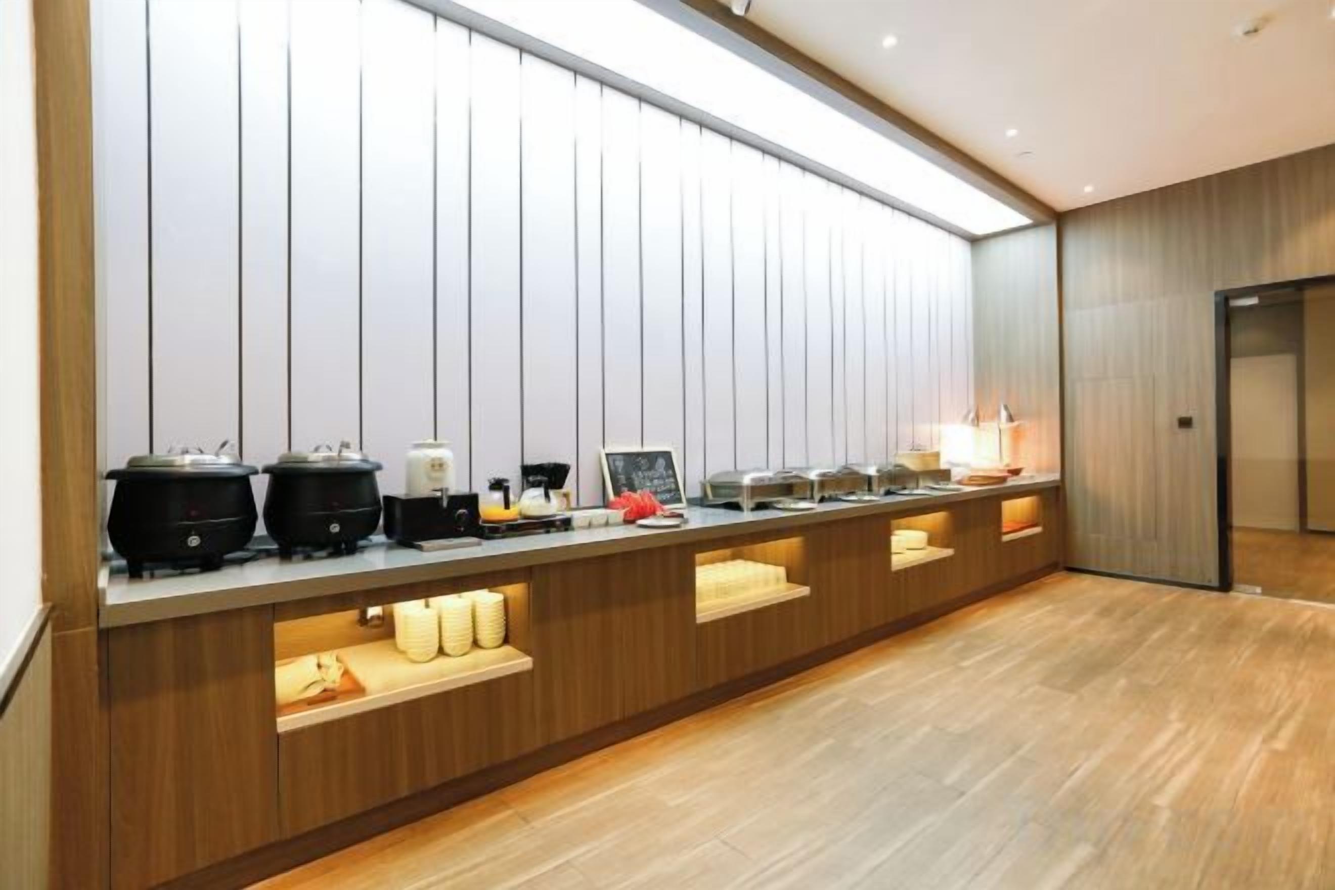 A modern hotel room with a long buffet counter, a wooden floor, and a large window.
