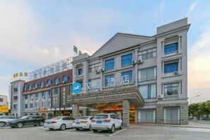 A hotel with a modern facade, multiple floors, and a parking lot with several cars. - HanTing Hotel (Cixi Longshan) (Cixi)