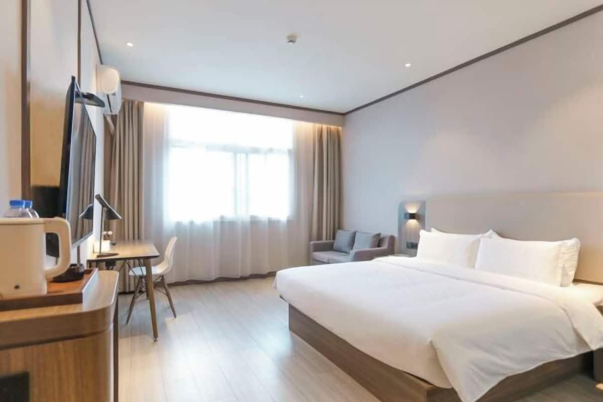 Una habitación de hotel moderna con una cama grande, un escritorio con una silla, una cafetera y una ventana con cortinas.