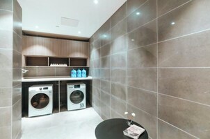 A modern bathroom with a black bathtub, two washing machines, and a shelf with toiletries.