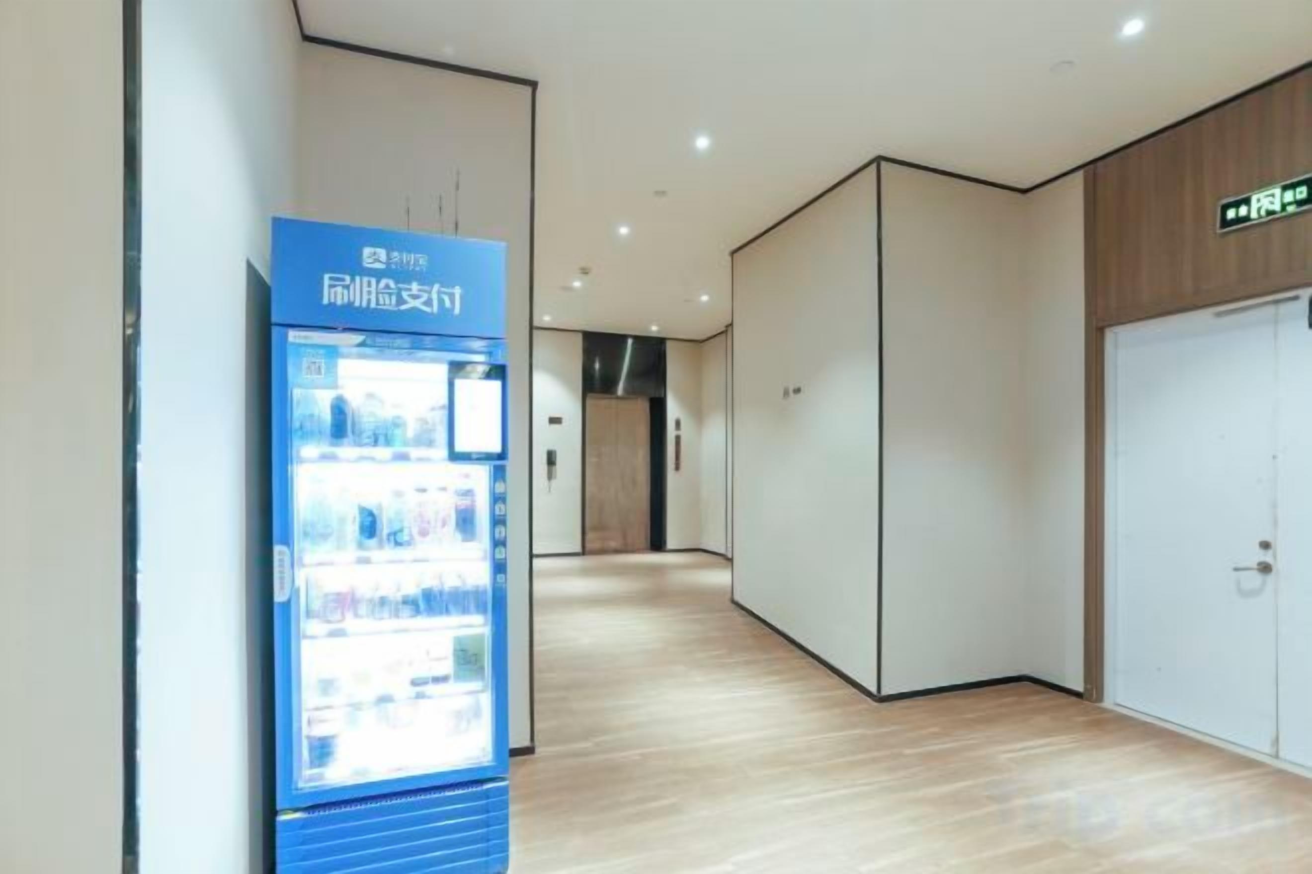 A corridor with a vending machine, wooden flooring, and a door on the right.