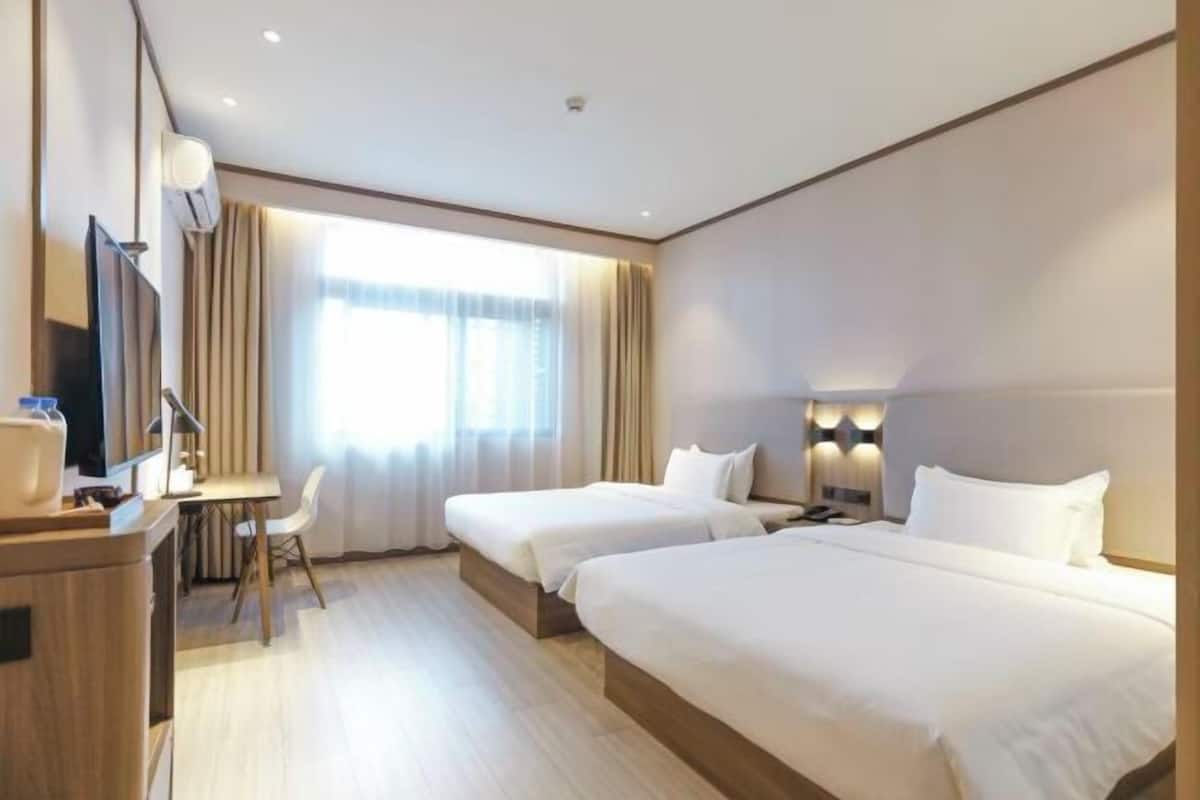 Habitación de hotel con dos camas, un escritorio, una silla, un televisor y una ventana con cortinas.