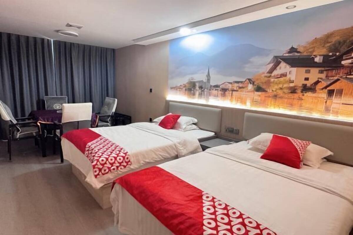 A hotel room with two beds, a desk, chairs, and a large window with a scenic view.