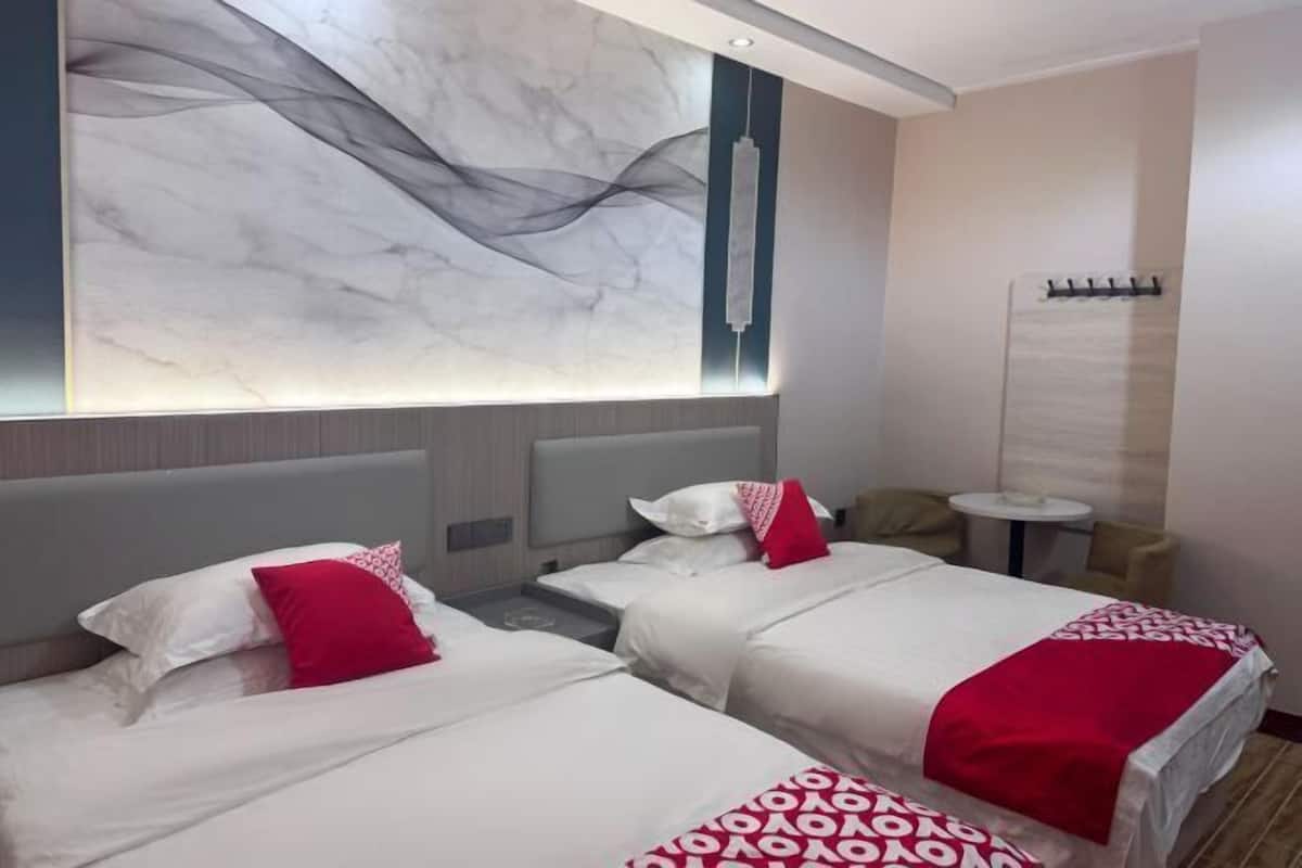 A hotel room with two beds, a marble wall, a small round table, and a wall-mounted hook.