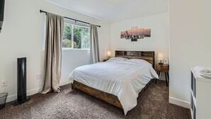 A bedroom with a bed, a window with curtains, a wall-mounted picture, a bedside table with a lamp, and a radiator. - Tranquil 2-bed SeaTac Hideaway! (SeaTac)