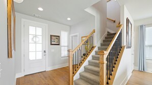 A spacious hallway with hardwood flooring, a wooden staircase with black railings, and white walls.