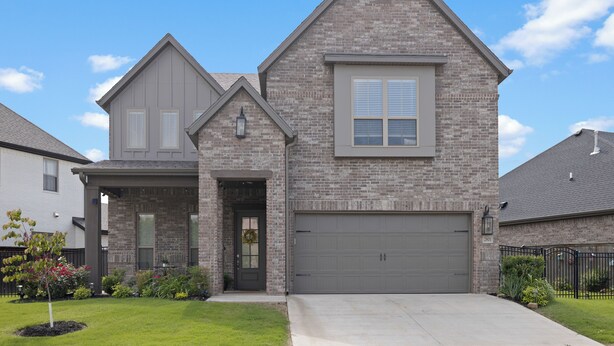 A two-story house with a brick facade, a front garage, and a well-maintained lawn.
