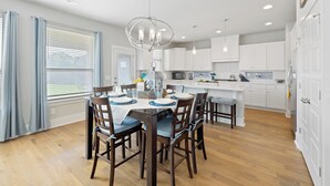 A modern kitchen with white cabinets, a central island, and a dining area with wooden chairs and a chandelier.