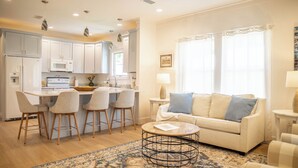 A modern kitchen with white cabinets, a central island with bar stools, and a dining area with a white table and chairs. - Perfect location in Ocean Springs! Walk to downtown & beach! Mother's Place (Ocean Springs)