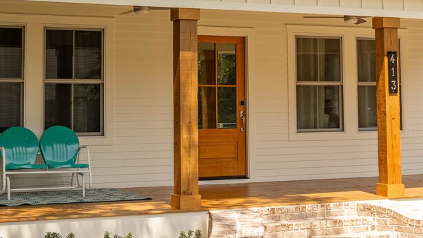 A white building with a wooden door, two windows, and a porch with green chairs. - Perfect location in Ocean Springs! Walk to downtown & beach! Mother's Place (Ocean Springs)