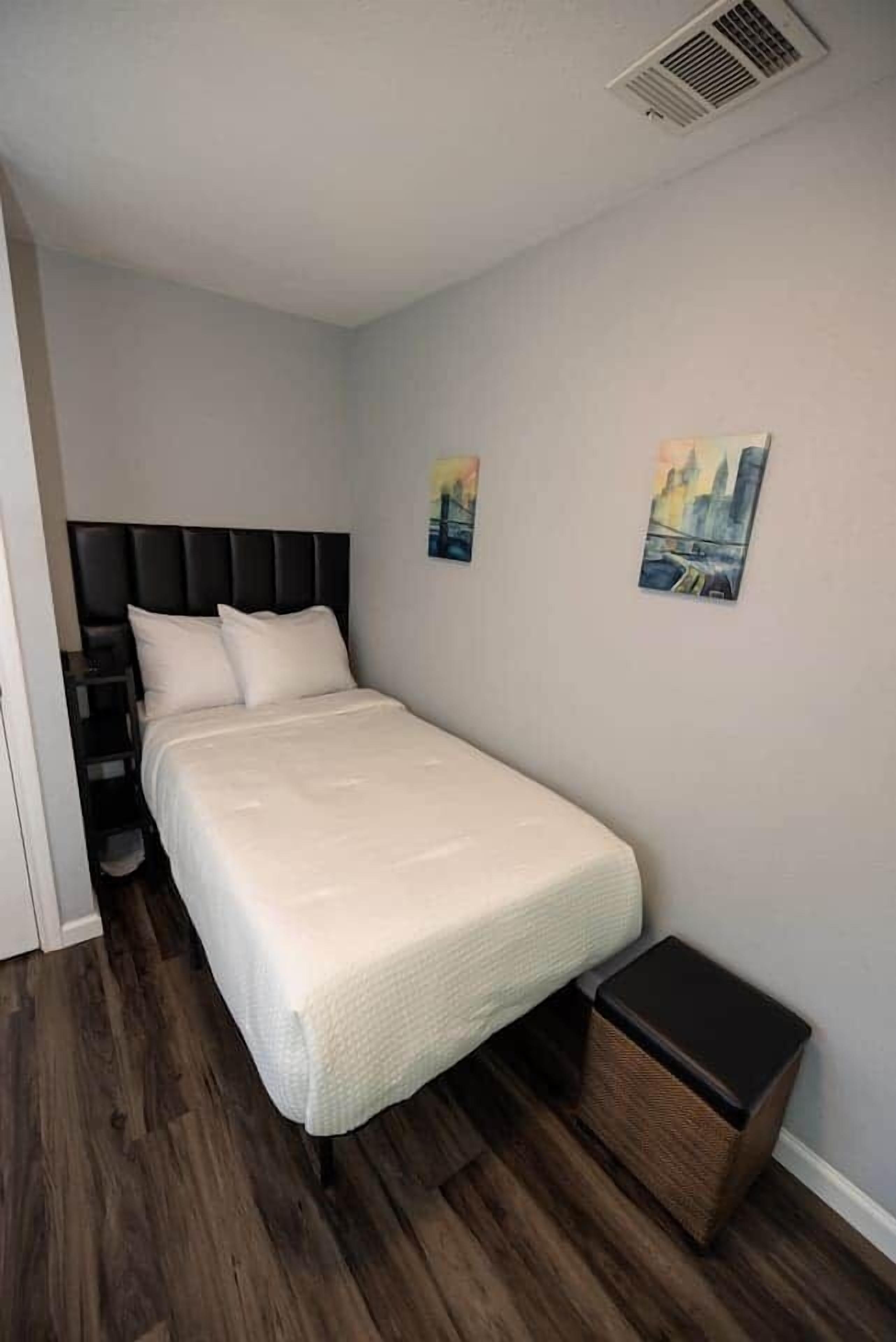 Ein Schlafzimmer mit einem Bett, einem Nachttisch, einem Mülleimer und zwei Wandbildern.