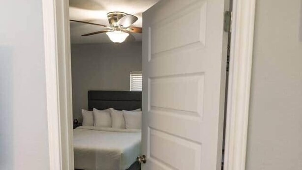 Une chambre à coucher avec un lit, un ventilateur de plafond et une porte donnant sur une autre pièce.