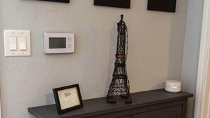 Une commode en bois foncé, ornée d’une petite maquette de la Tour Eiffel, d’une pancarte encadrée indiquant « WiFi » et de trois petits miroirs carrés fixés au mur.