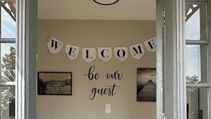 A hallway with a 'WELCOME' sign and a 'be our guest' sign on the wall. - Riverside Retreat 2 ~ One Story ~ 3bd/2ba ~ Steps to the River & Main St (Madison)