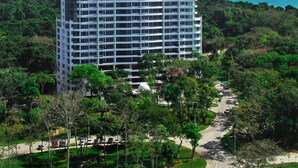 A high-rise hotel with a central dome and multiple floors, surrounded by lush greenery and a clear view of the ocean. - 06E Floor to Ceiling Oceanview Resort  (Veracruz)
