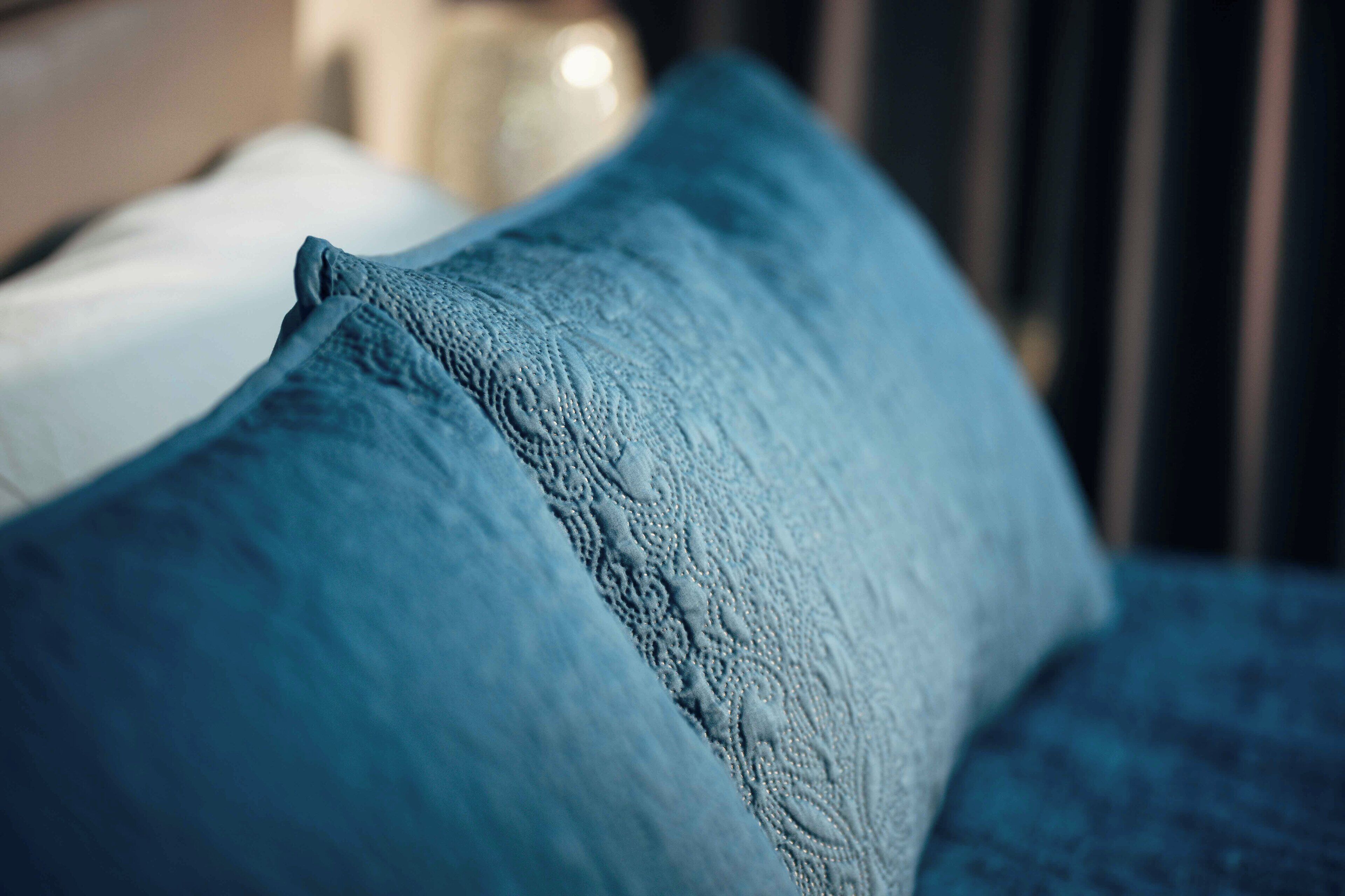 A close-up of a blue textured pillow on a bed.