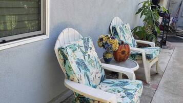 Two white Adirondack chairs with floral upholstery, a small table with a pumpkin decoration, and a potted plant on a concrete patio.