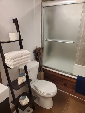 Une salle de bain moderne avec des toilettes blanches, un porte-serviettes noir sur lequel sont pliées des serviettes, et une douche à parois de verre.