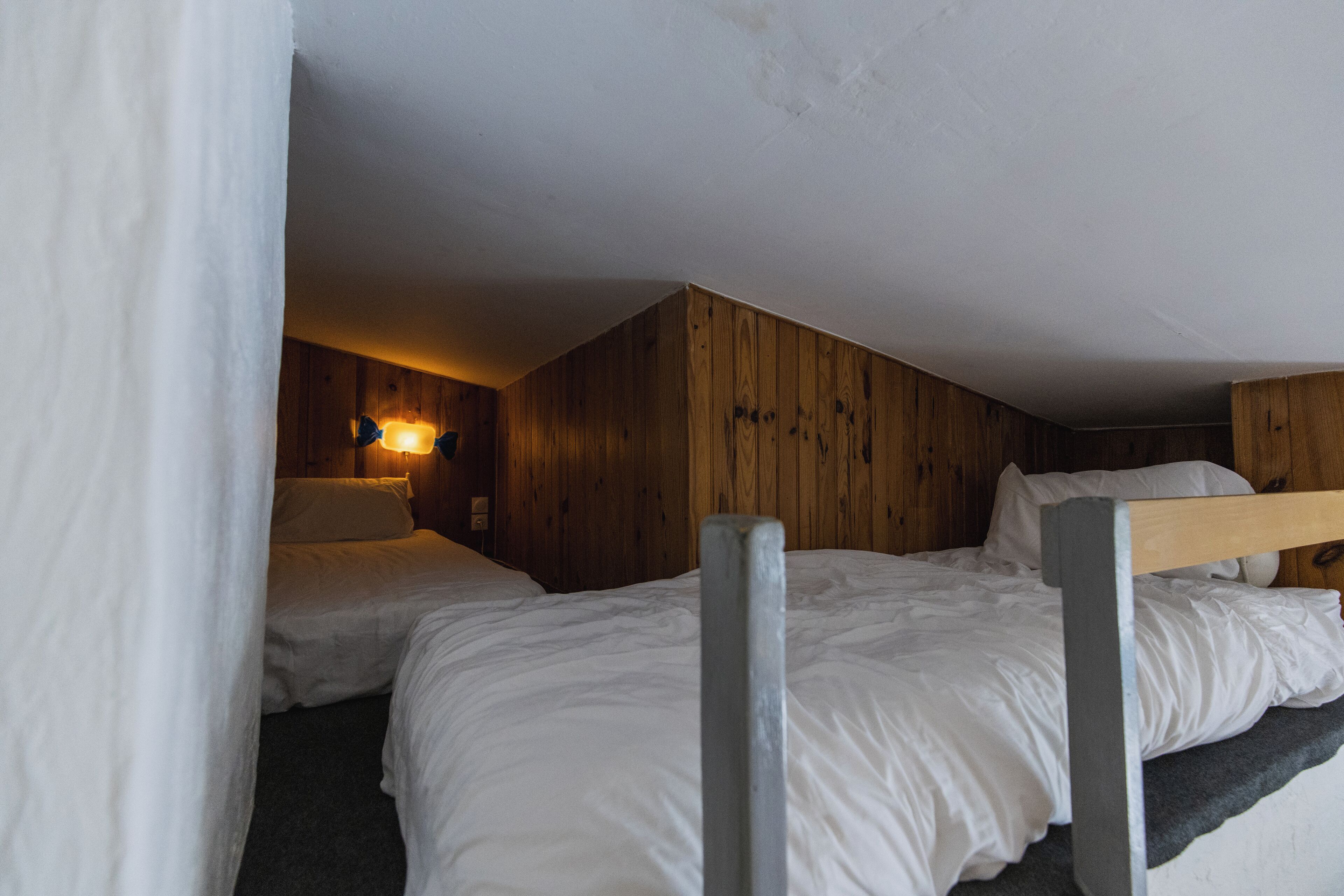 Une chambre avec deux lits, des murs en bois et un luminaire fixé au mur.