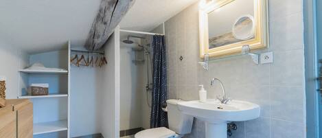 Ein Badezimmer mit Toilette, Waschbecken und Dusche. Handtuchhalter und Ablagefläche für Toilettenartikel vorhanden.