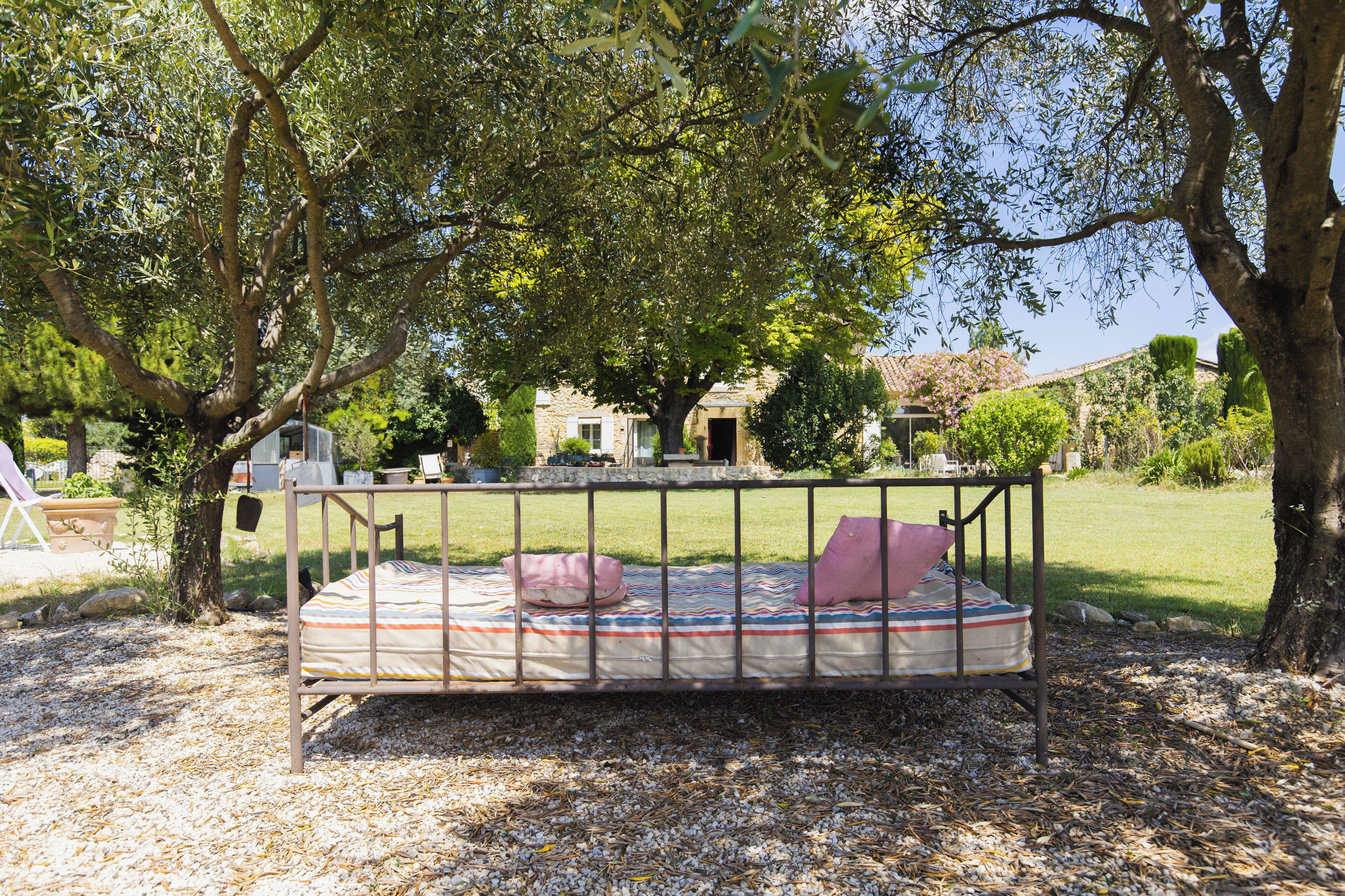 A bed with a metal frame and a striped mattress, surrounded by trees and a grassy area.