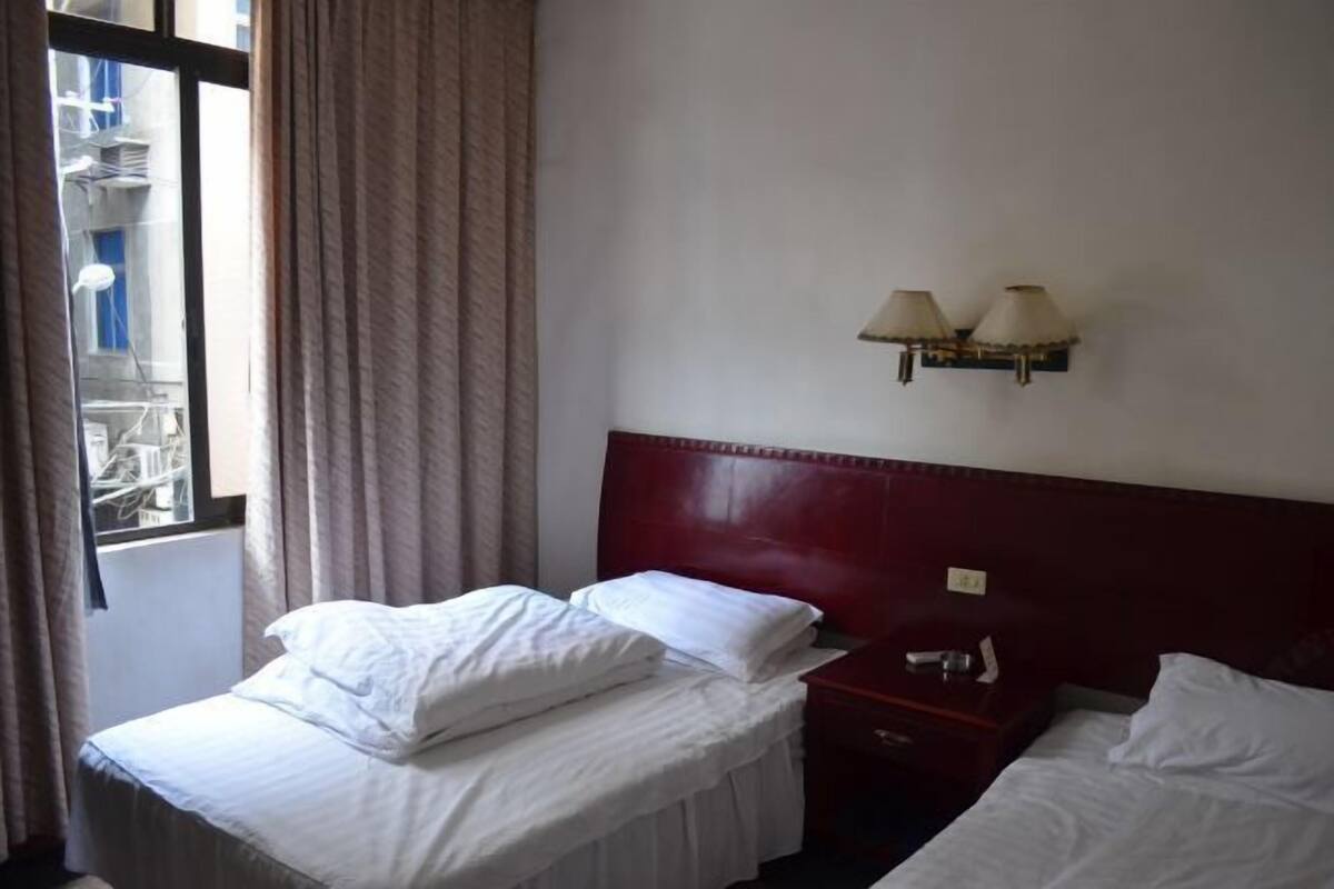 Une chambre d’hôtel avec deux lits, une fenêtre avec des rideaux et une lampe fixée au mur.