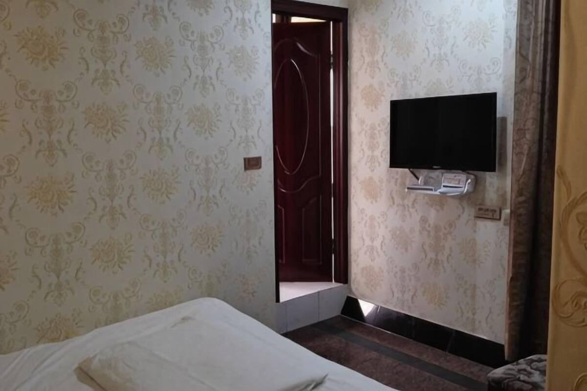Une chambre d’hôtel avec un lit, un téléviseur fixé au mur et une porte donnant sur une autre pièce.