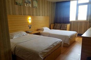 Ein Hotelzimmer mit zwei Betten, einem Nachttisch mit Telefon, einer Wandlampe und einem Fenster mit blauen Vorhängen.