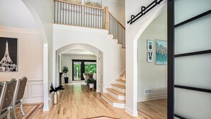 Un hallo espacioso con pisos de madera, una escalera y un comedor con sillas y una mesa.