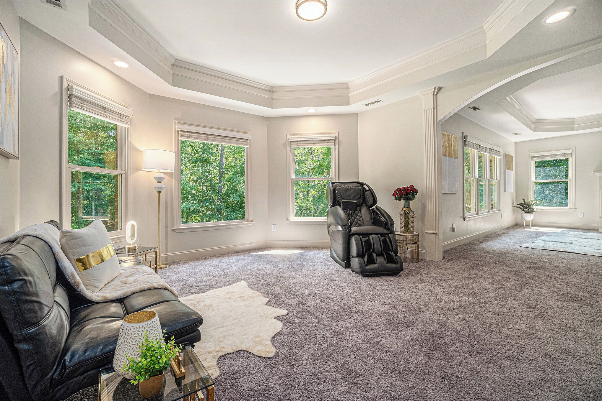 A spacious room with a large window, a massage chair, a leather sofa, and a white rug.