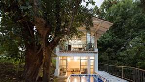 A modern house with a glass facade, a pool, and a large tree in the foreground. - Casa Paraíso, Valle de Bravo. (Valle de Bravo)