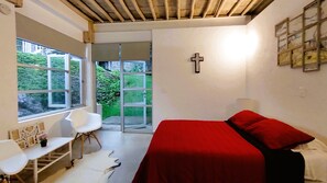 A bedroom with a bed, a chair, a desk, and a window with a view of greenery.