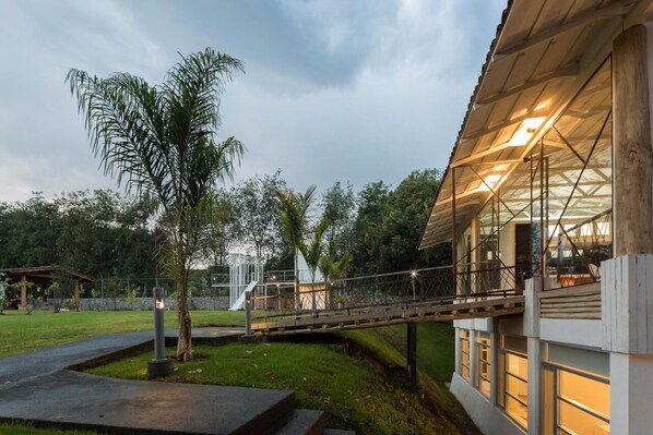 A modern building with a glass facade, a wooden deck, and a pathway leading to a covered area.