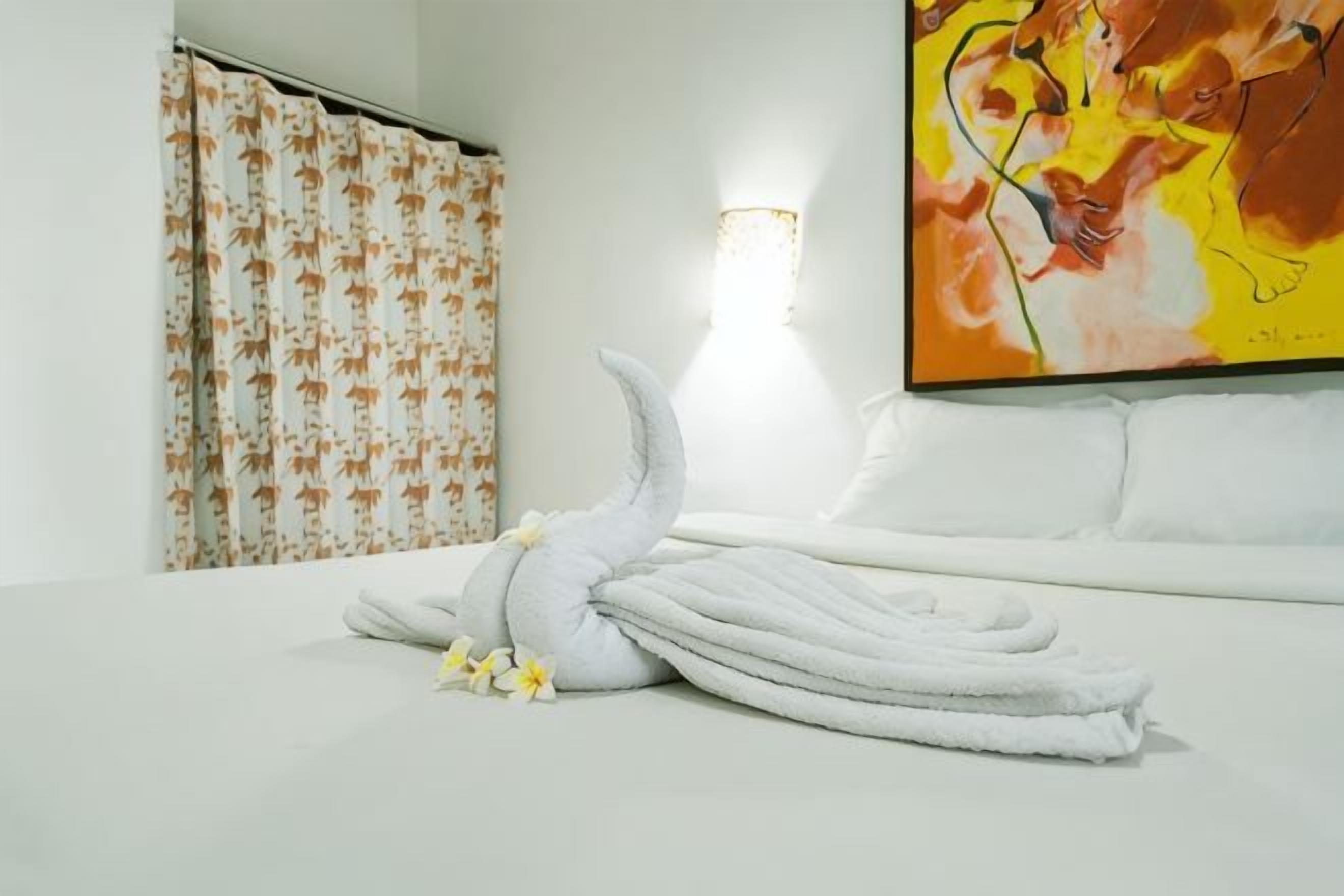 A hotel room with a neatly made bed, a wall-mounted artwork, and a shower curtain with a leaf pattern.