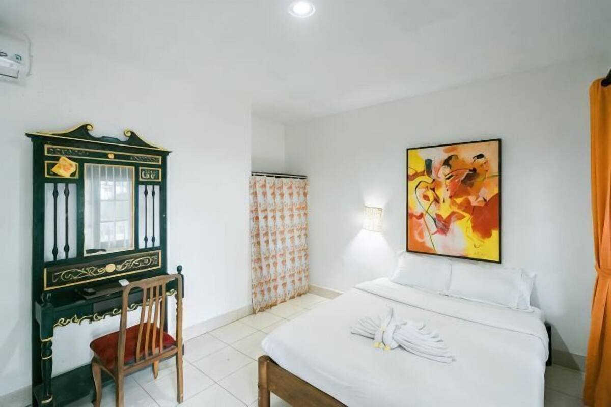Una habitación de hotel con cama, escritorio, silla, un cuadro y cortina.