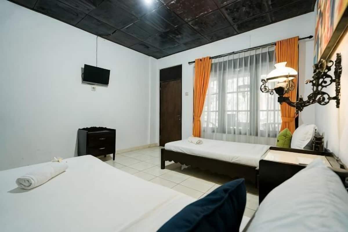 A room with two beds, a TV, a desk, and a window with curtains.