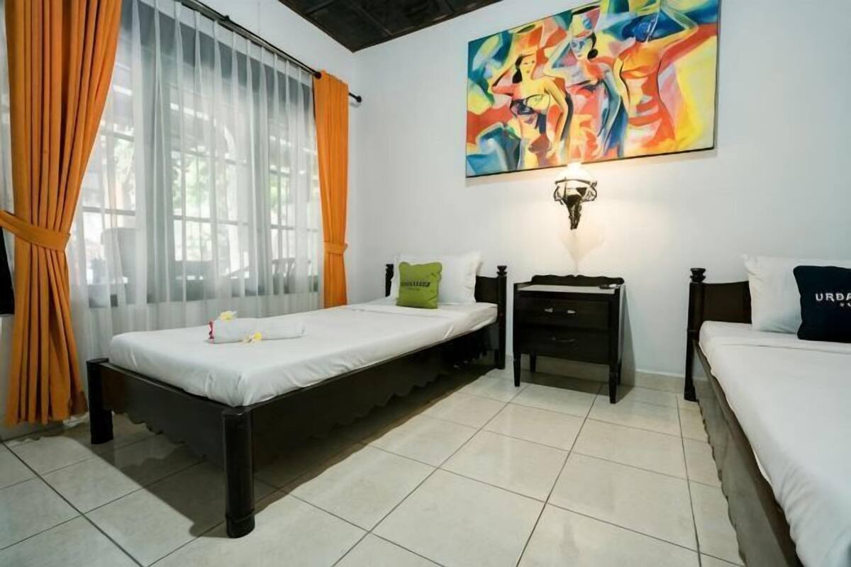 Un dormitorio con cama, mesita de noche, lámpara y un cuadro en la pared.
