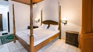 Un lit à baldaquin avec une tête de lit en bois, deux lampes fixées au mur et une petite table de chevet en bois.