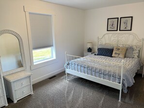 A bedroom with a white metal bed frame, a white dresser with drawers, a large mirror, a window with blinds, and two framed pictures on the wall. - Entire home in Valier, Montana (Valier)