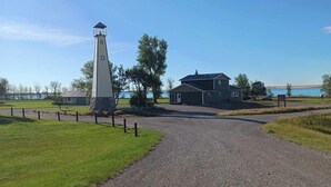 Un faro, una casa y un camino de grava que lleva a una masa de agua.