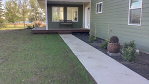 Una casa moderna con un porche cubierto, un pequeño jardín y un sendero de concreto que lleva a la entrada.