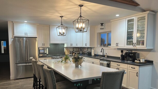 Una cocina moderna con gabinetes blancos, electrodomésticos de acero inoxidable y una isla central con asientos.