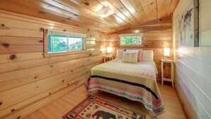A cozy cabin bedroom with a wooden ceiling, two windows, a bed with a colorful quilt, bedside tables with lamps, and a rug on the floor. - Rustic Cabin w/ Patio: 8 Mi to Kings Canyon Park (Miramonte)