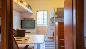 Ein kompakter Raum mit Schreibtisch, Stuhl, Laptop und Fernseher. Eine Treppe führt zu einer erhöhten Ebene.