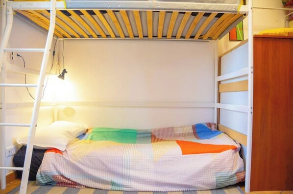 A bunk bed with a ladder, a colorful quilt, and a desk with a lamp.
