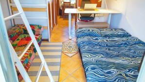 Ein kleines Zimmer mit Etagenbetten, einem Schreibtisch mit einem Laptop und einem gemusterten Teppich.