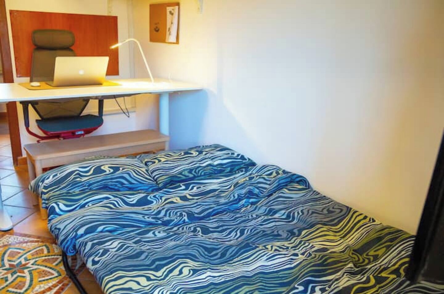 A small room with a bed, a desk with a laptop, a chair, and a small table.